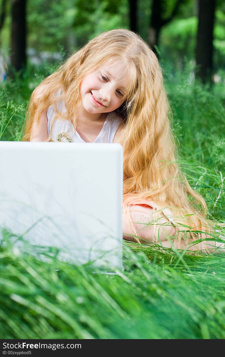 Serious looking little girl with laptop in green grass