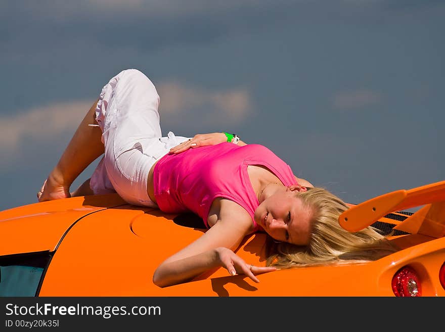 A female model laying on an orange super car. A female model laying on an orange super car