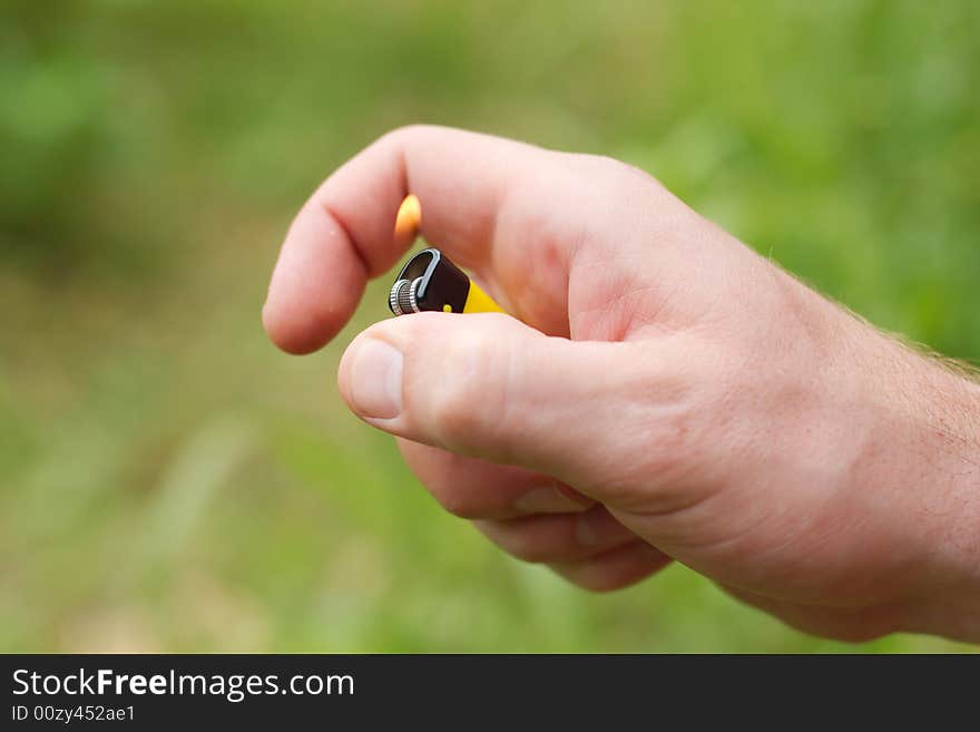 Hand holding yellow lighter with flame, outdoors. Hand holding yellow lighter with flame, outdoors