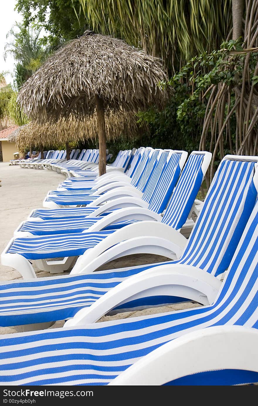 Blue and white striped lounge chairs around a luxury resort swimming pool. Blue and white striped lounge chairs around a luxury resort swimming pool