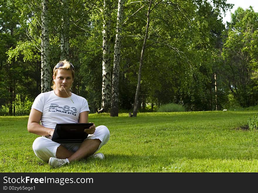 Casual man works on laptop on the grass