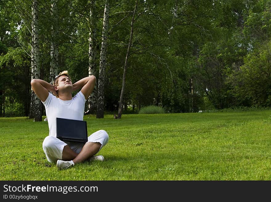 Casual man works on laptop on the grass