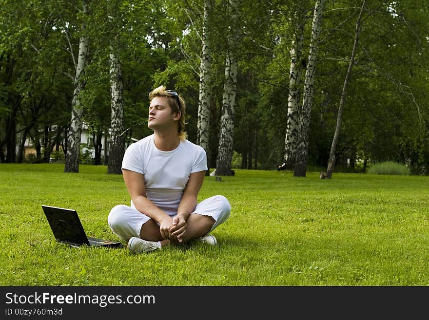 Casual man works on laptop on the grass