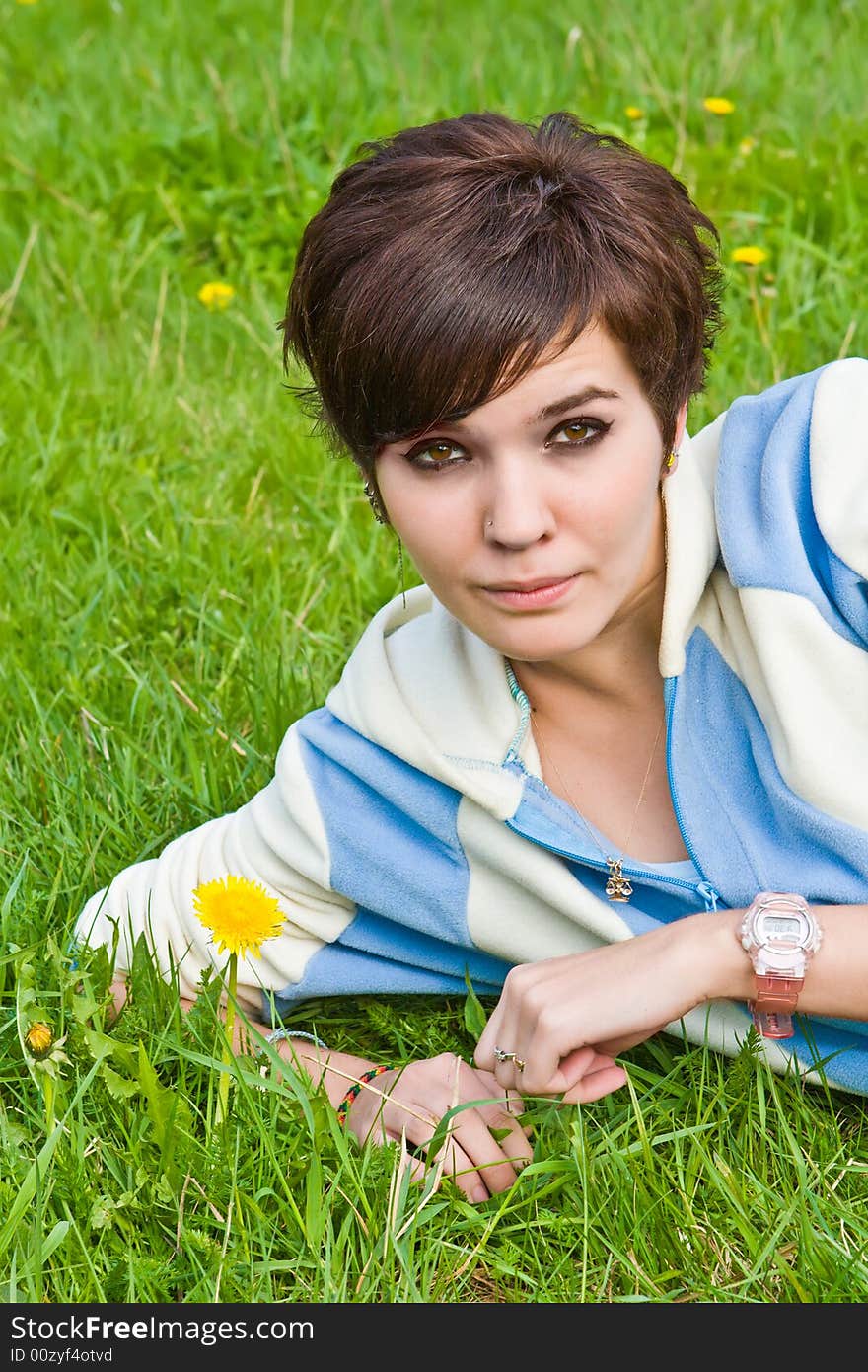 Girl lays on a green grass with yellow dandelions. Girl lays on a green grass with yellow dandelions