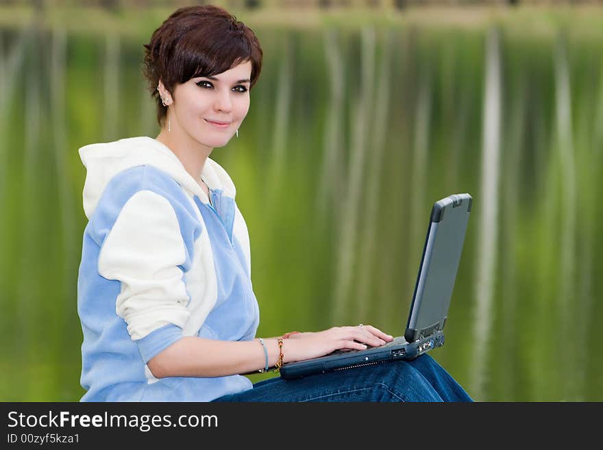 Attractive girl with a portable computer sits on coast of lake