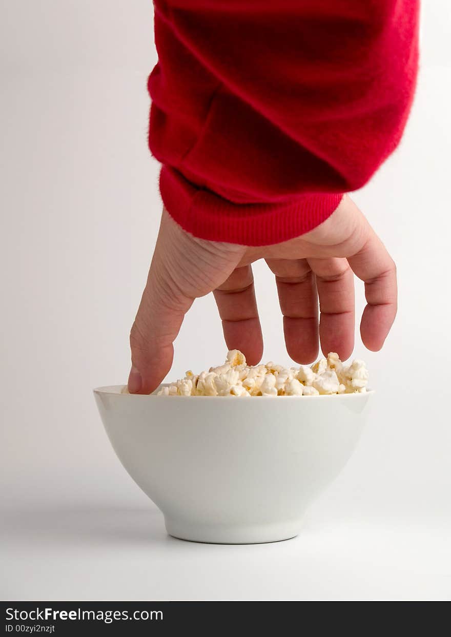 A hand trying to reach some popcorns from a bowl.