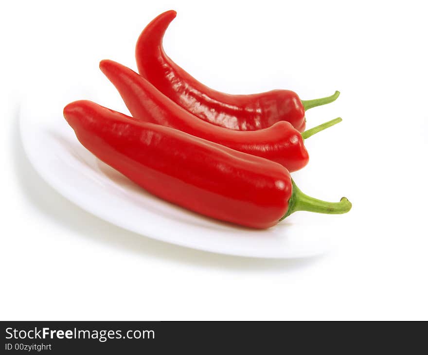 Three fresh red chili peppers on white plate and isolated on white background. Three fresh red chili peppers on white plate and isolated on white background