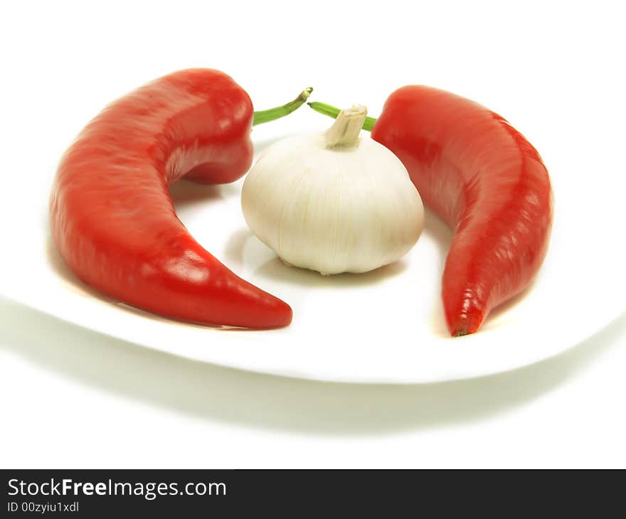 Two fresh chili peppers and a bulb of garlic on a white plate and isolated on white background. Two fresh chili peppers and a bulb of garlic on a white plate and isolated on white background