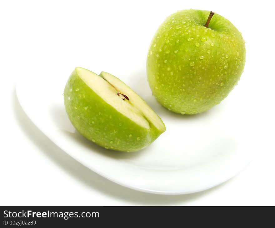 A half and a whole fresh ripe green apple with water drops on white plate and isolated on white background. A half and a whole fresh ripe green apple with water drops on white plate and isolated on white background