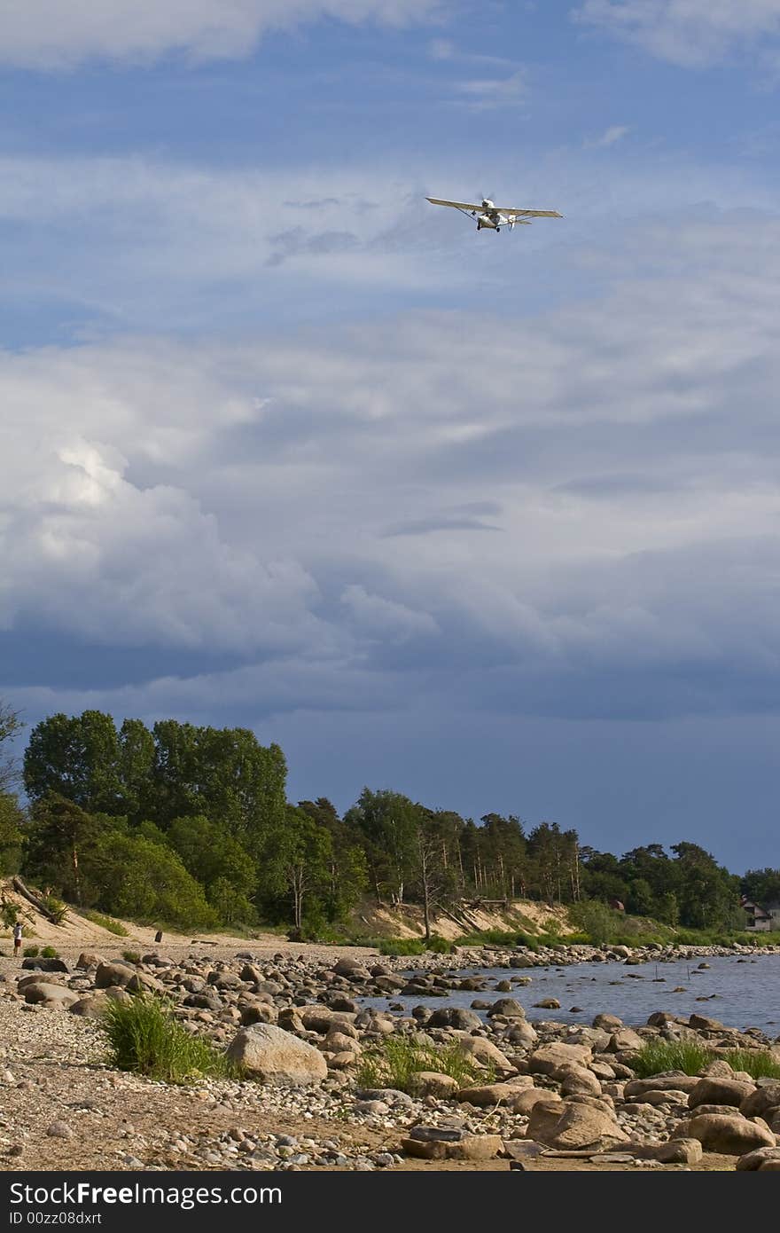 Plane, flying in the blue, cloudy sky above the green forest and stone sea coast. Plane, flying in the blue, cloudy sky above the green forest and stone sea coast