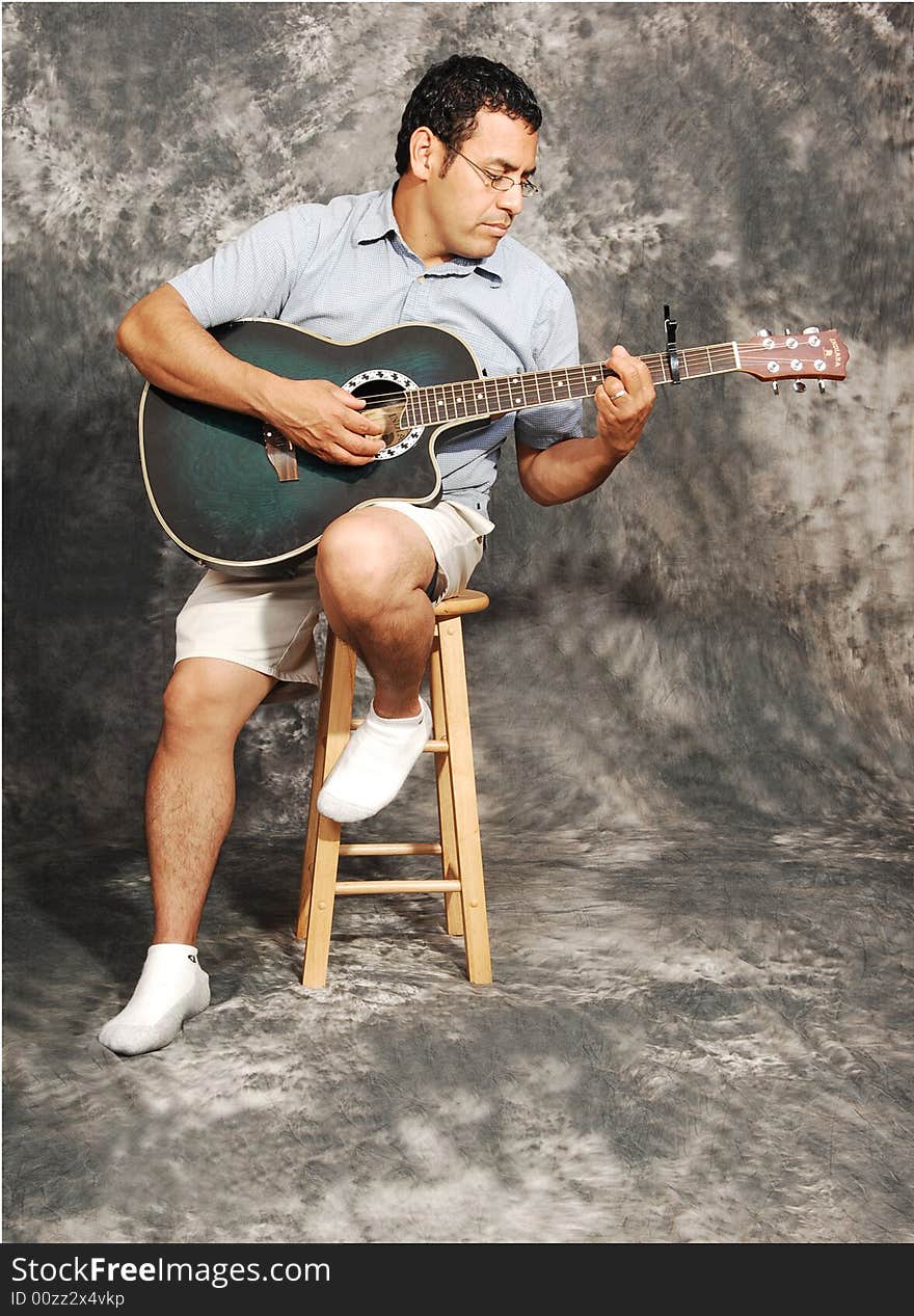 An man in shorts sitting on a chair with an green guitar for a black 
and white background. An man in shorts sitting on a chair with an green guitar for a black 
and white background.