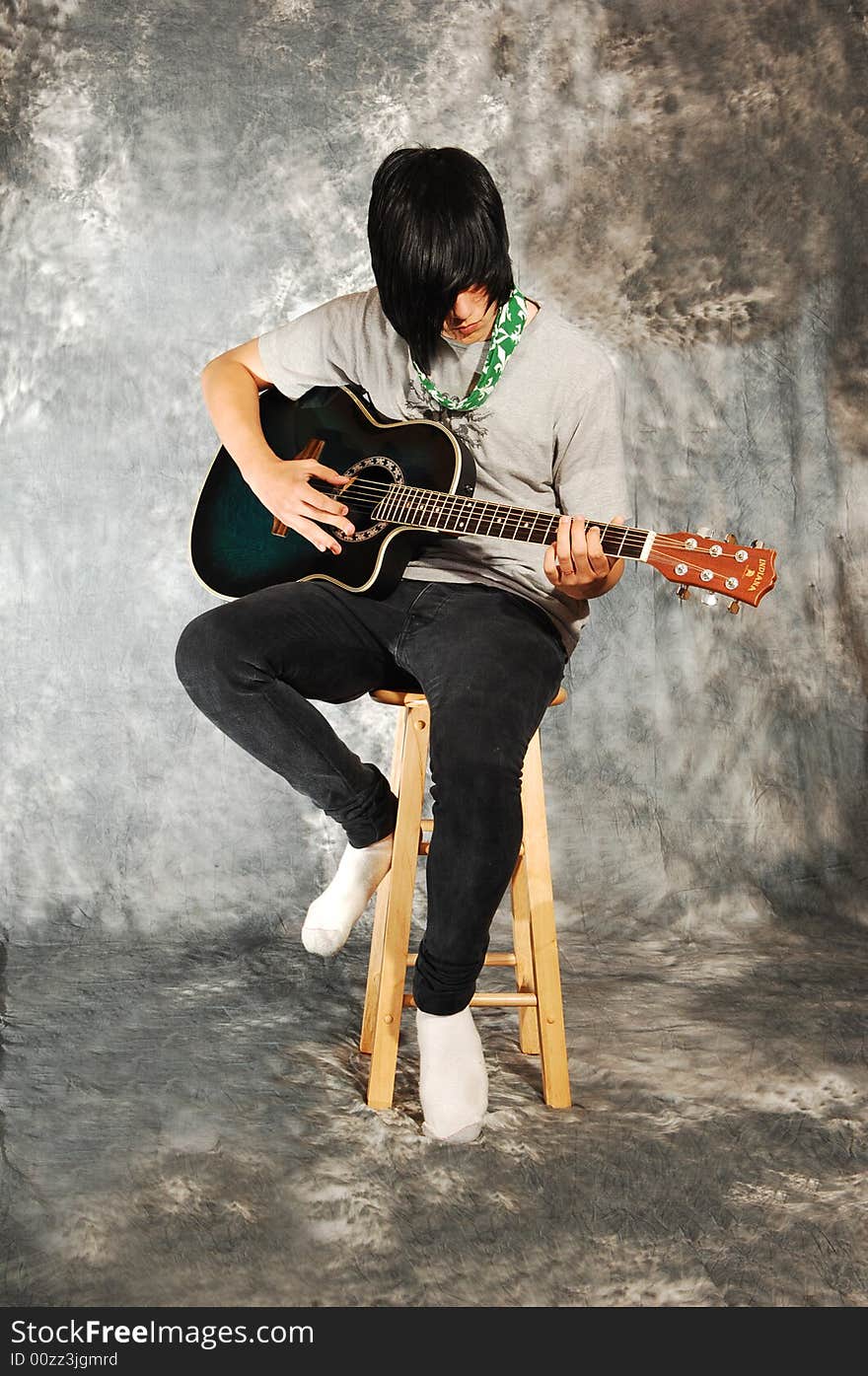 An boy in black jeans sitting on a chair with an green guitar for a black 
and white background. An boy in black jeans sitting on a chair with an green guitar for a black 
and white background.