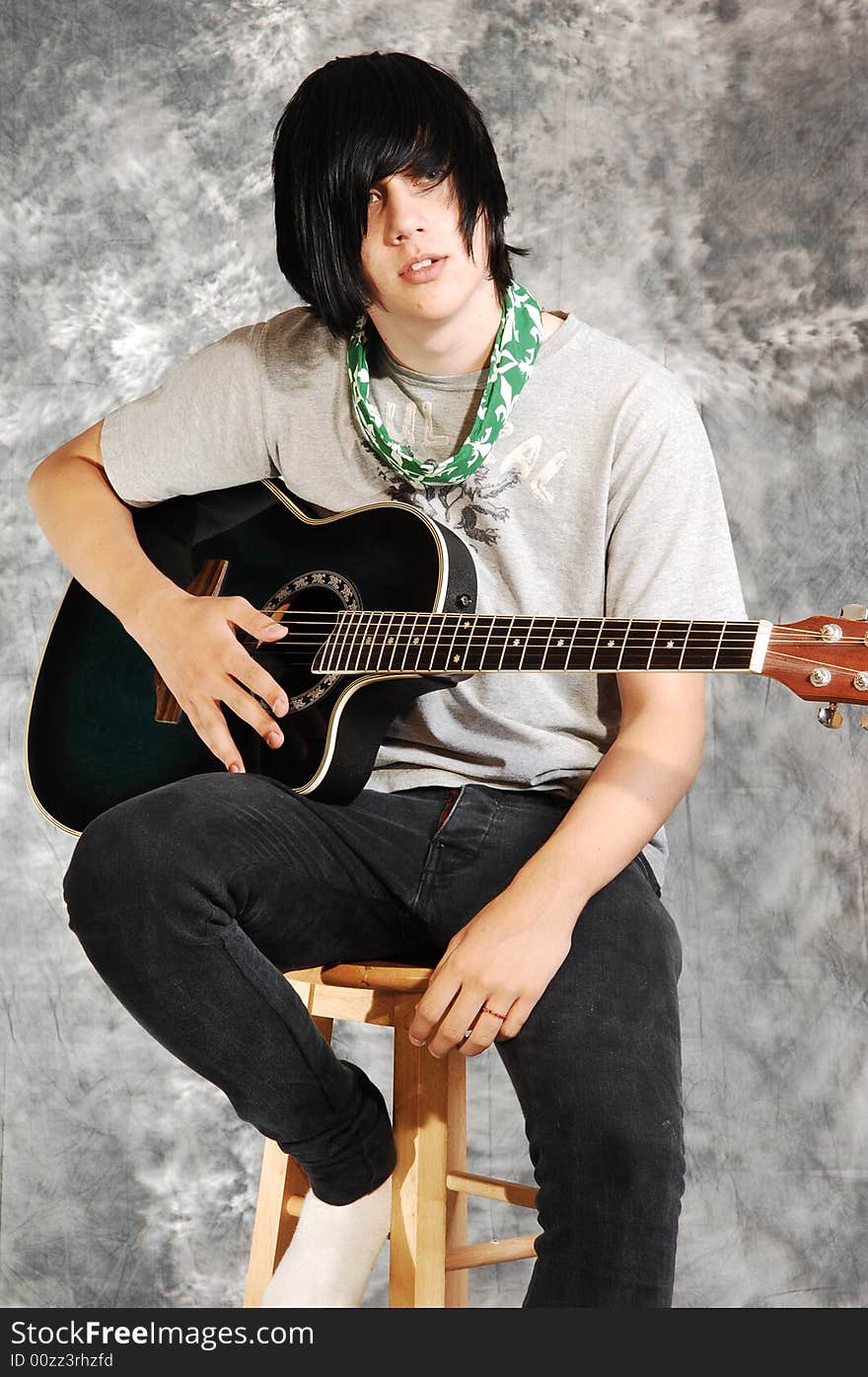 An boy in black jeans sitting on a chair with an green guitar for a black 
and white background. An boy in black jeans sitting on a chair with an green guitar for a black 
and white background.