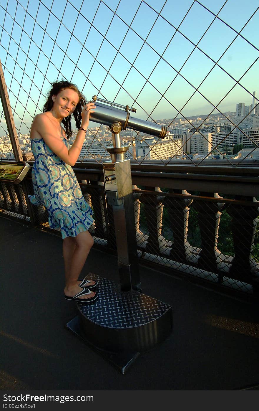 A young woman observing the view of Paris through a telescope from on the Eiffel Tower. A young woman observing the view of Paris through a telescope from on the Eiffel Tower.