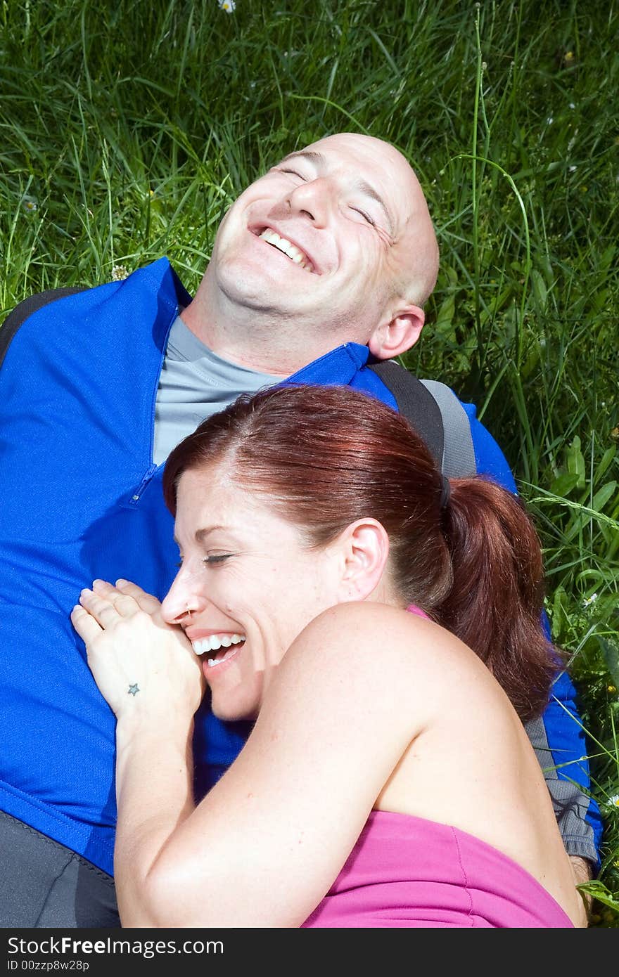 Happy couple sitting on the grass laughing. Vertically framed photograph. Happy couple sitting on the grass laughing. Vertically framed photograph