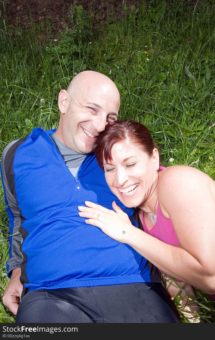 Happy couple sit on the grass in the park. She is leaning on his shoulder and they are laughing. Vertically framed photograph. Happy couple sit on the grass in the park. She is leaning on his shoulder and they are laughing. Vertically framed photograph