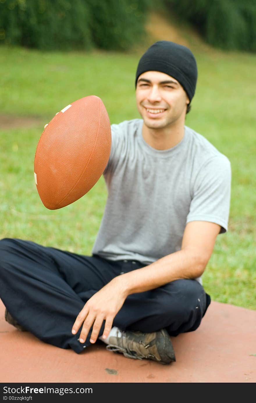 Man Sitting in Park Holding Football - Vertical