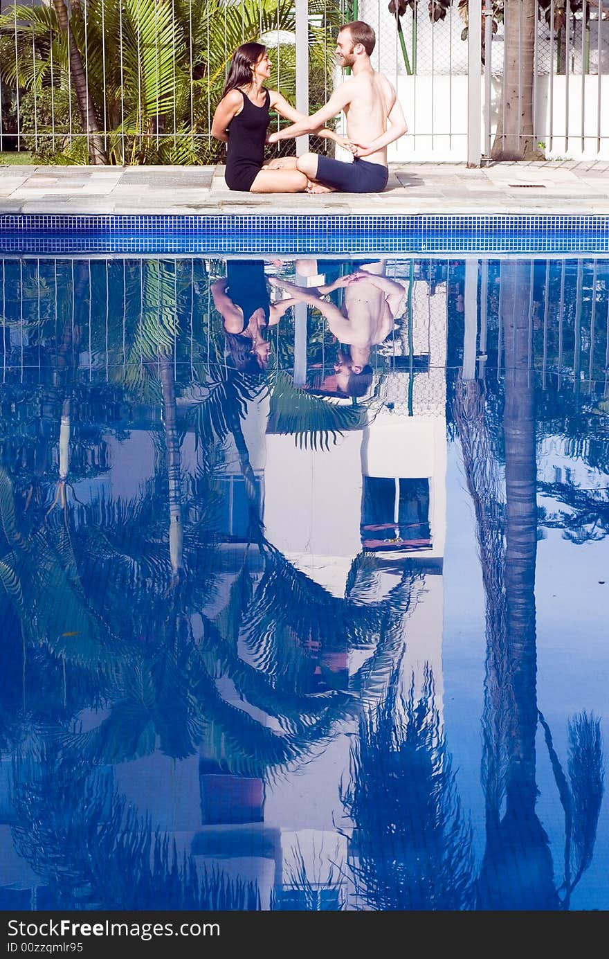 A couple, sit down by the pool, crossing arms, stretching, smiling at each other - vertically framed. A couple, sit down by the pool, crossing arms, stretching, smiling at each other - vertically framed