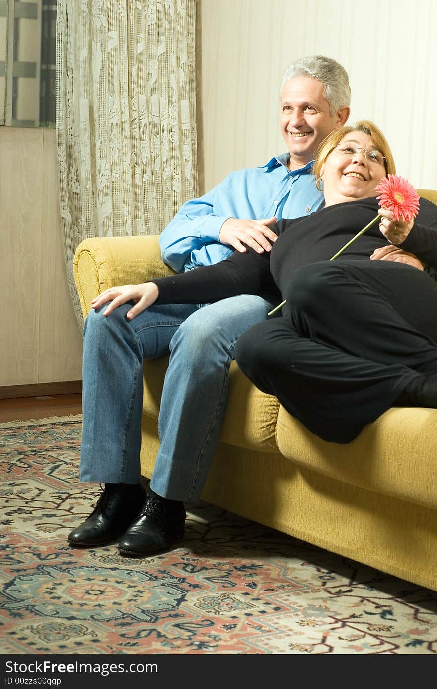 A couple smiling on a couch.  The woman is laying on his lap and holding a flower. Vertically framed shot. A couple smiling on a couch.  The woman is laying on his lap and holding a flower. Vertically framed shot.