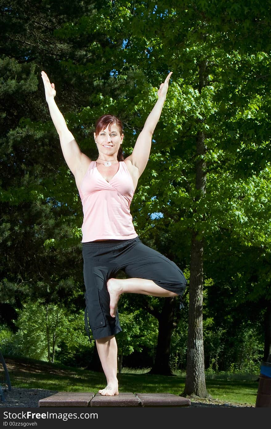 Woman smiles as she does a yoga pose in the park. Vertically framed photograph. Woman smiles as she does a yoga pose in the park. Vertically framed photograph.