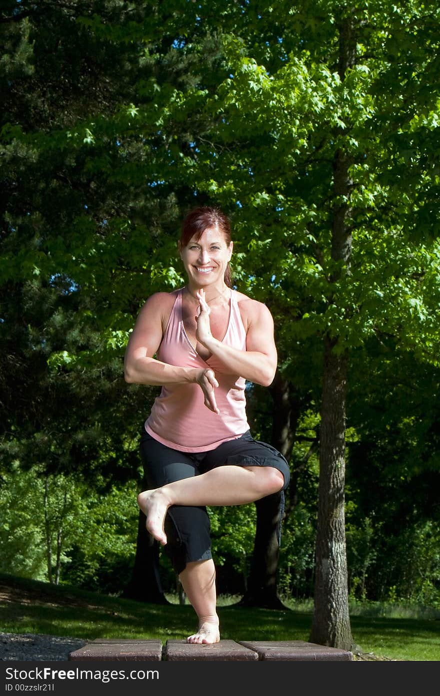 Physically fit woman standing on picnic table in the park. Posed in seated yoga position and smiling. Vertically framed shot. Physically fit woman standing on picnic table in the park. Posed in seated yoga position and smiling. Vertically framed shot.