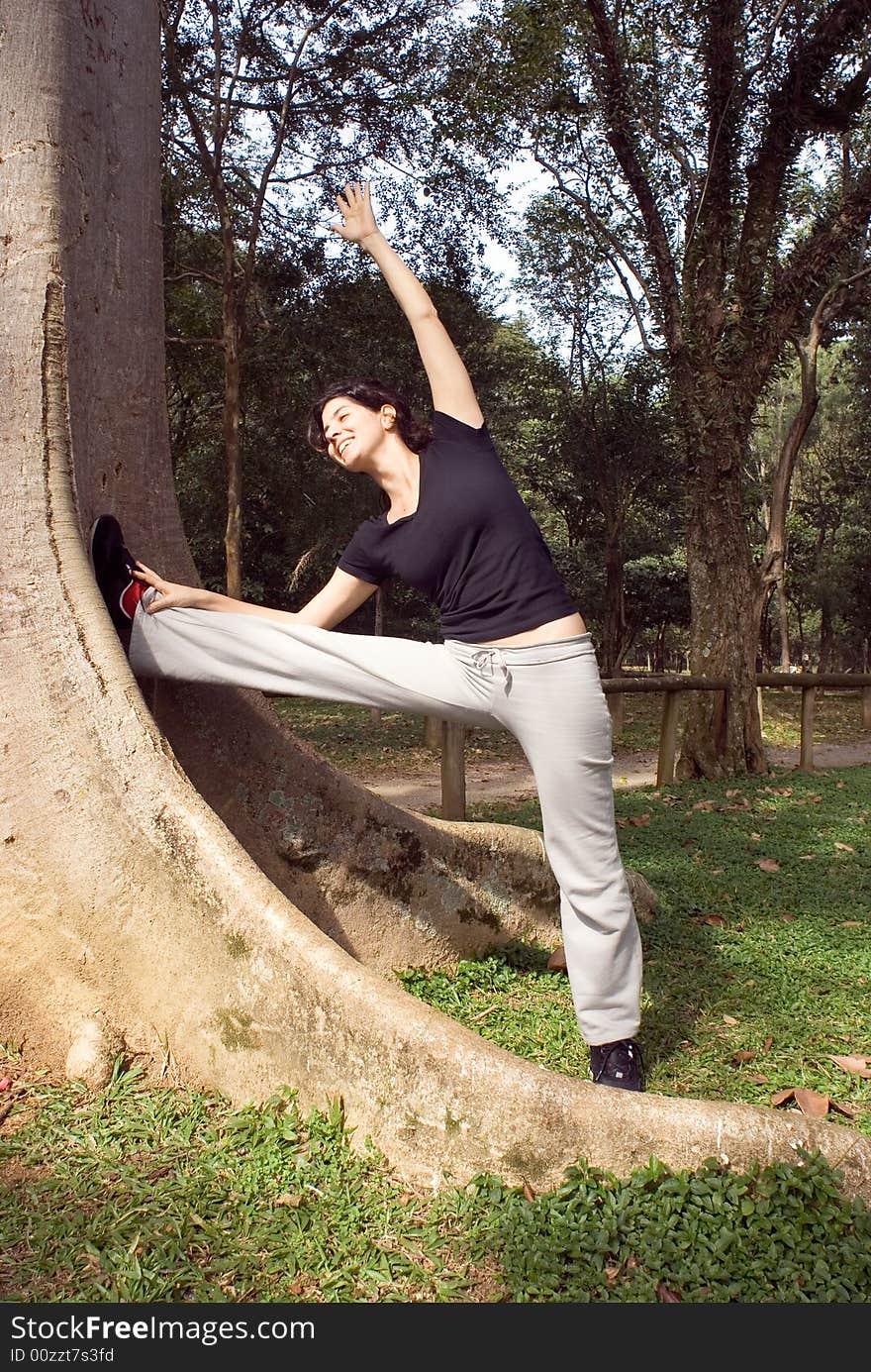 Woman Stretching Her Leg by a Tree - Vertical