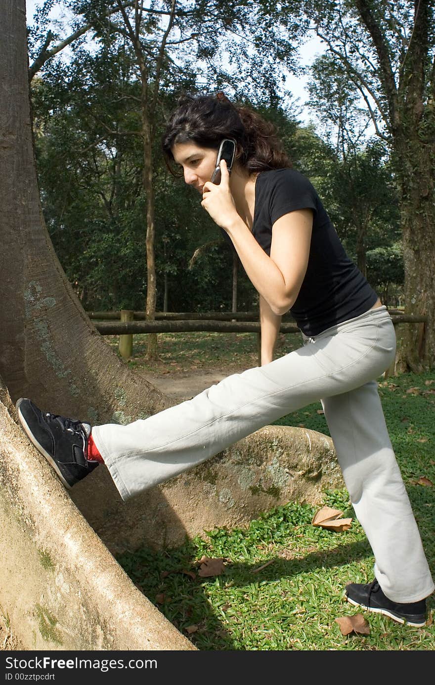 A young, attractive woman is standing next to a tree.  She is looking at her foot, and stretching her leg on the tree.  Vertically framed photo. A young, attractive woman is standing next to a tree.  She is looking at her foot, and stretching her leg on the tree.  Vertically framed photo.