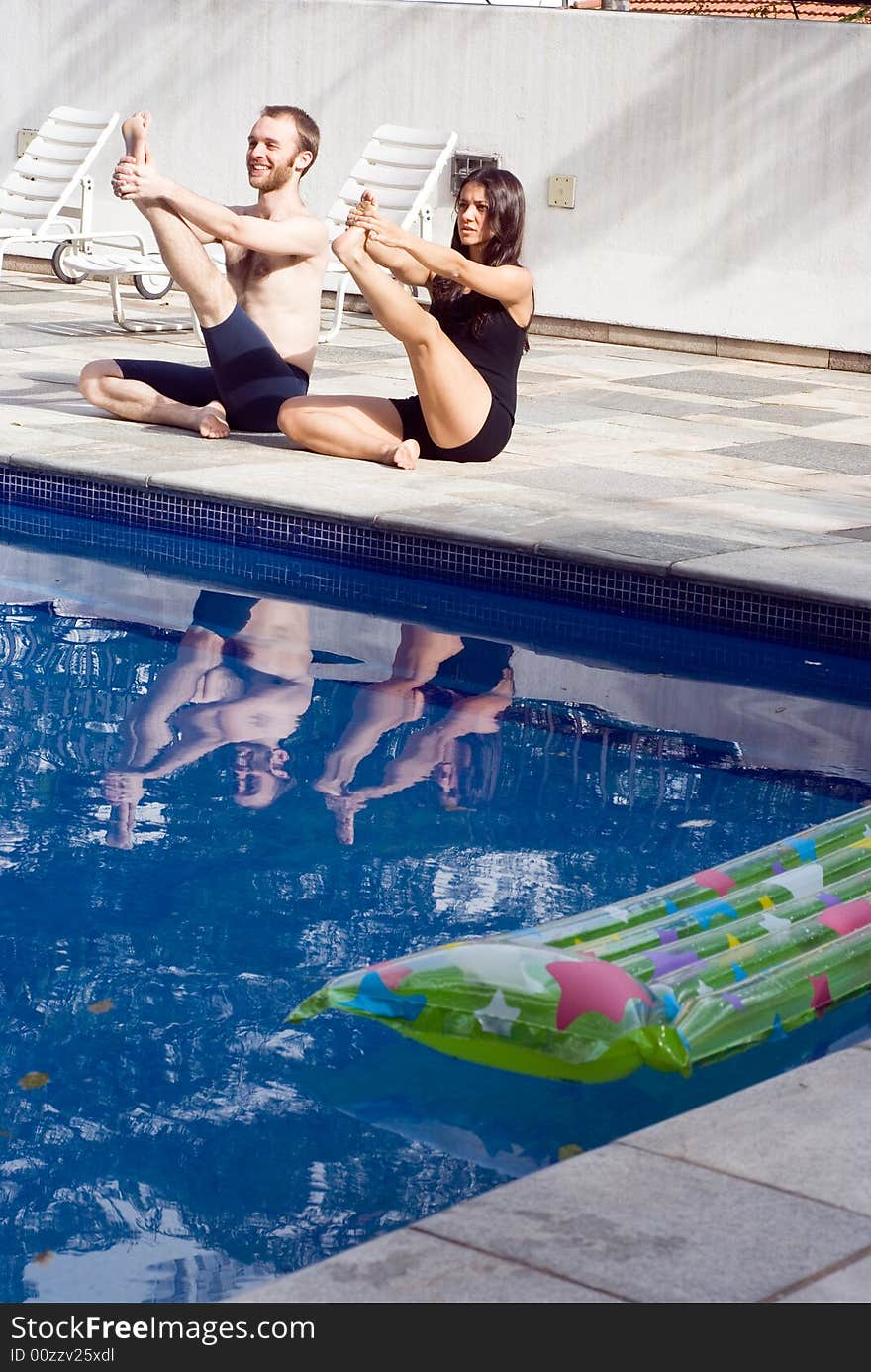 A couple stretching their legs, smiling ,by the poolside, in their swimsuits - vertically framed. A couple stretching their legs, smiling ,by the poolside, in their swimsuits - vertically framed