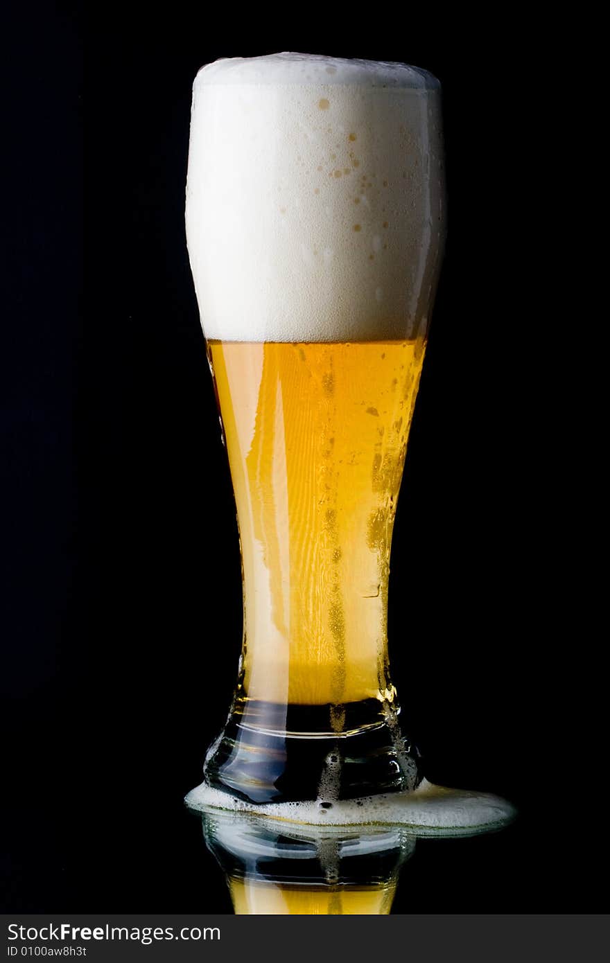 Fresh foamy beer in a glass on a black background.