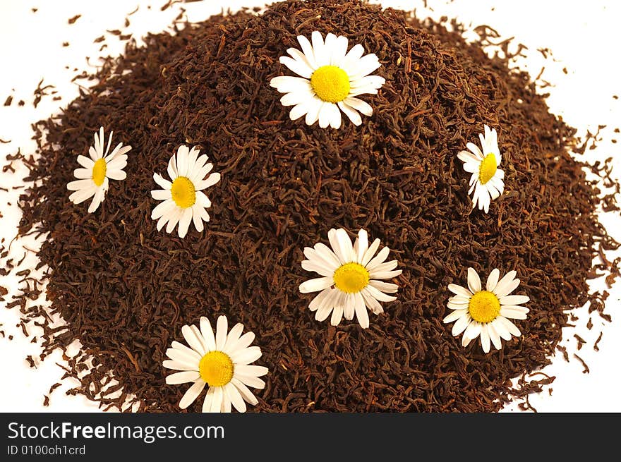 Heap of black tea and chamomile blossoms isolated on white