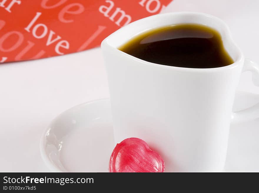 Freshly brewed coffee in white heart shape cup with words of love in background