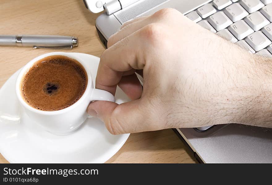 Close up of a hand taking a cup of coffee over a laptop. Close up of a hand taking a cup of coffee over a laptop.