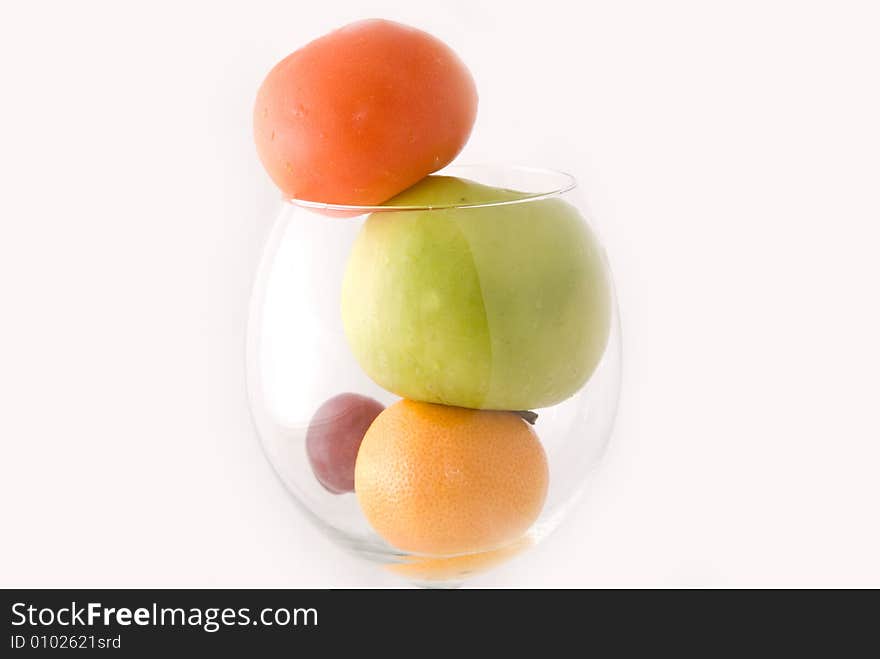 A cup of fresh fruits, including red tomato, green apple, orange, and red grape, on white background