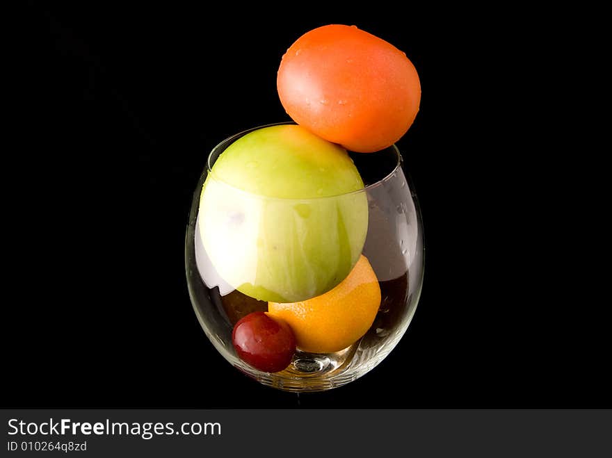 A cup of fresh fruits, including red tomato, green apple, orange, and red grape, on black background