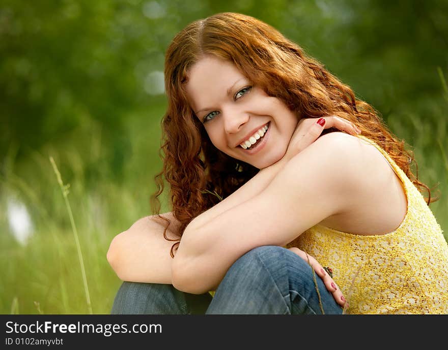 A smiling girl sits on a background of trees and grasses. A smiling girl sits on a background of trees and grasses