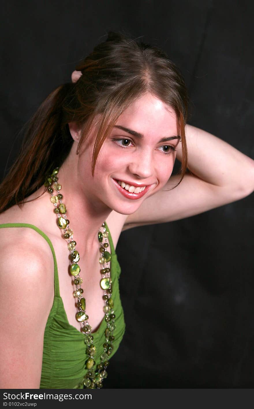 Portrait of a smiling beautiful teenage girl with green beads on her neck is busy styling her hair against black back-ground. Portrait of a smiling beautiful teenage girl with green beads on her neck is busy styling her hair against black back-ground.