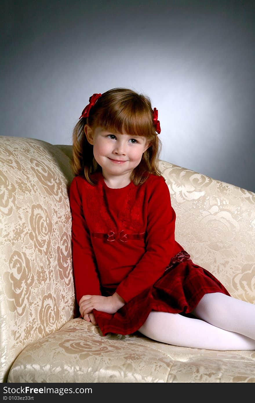 Cute preschool aged girl in red dress on couch looking up and away as if she is hiding something. Cute preschool aged girl in red dress on couch looking up and away as if she is hiding something