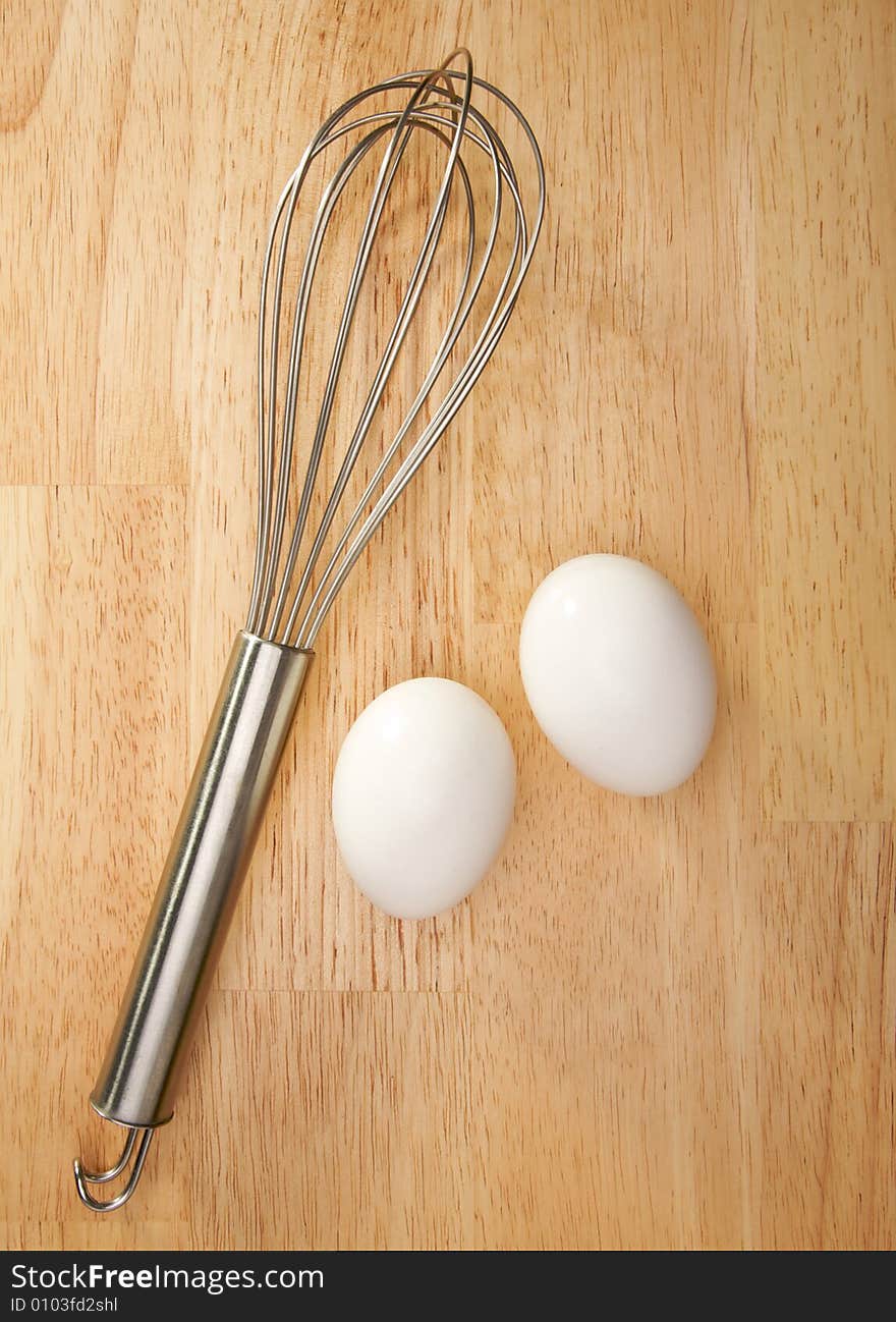 Whisk and Eggs on a wooden background.