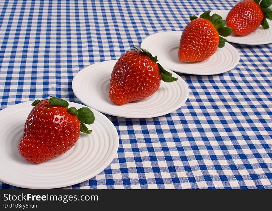 Delicious fresh strawberries served on individual plates on a blue gingham tablecloth. Delicious fresh strawberries served on individual plates on a blue gingham tablecloth