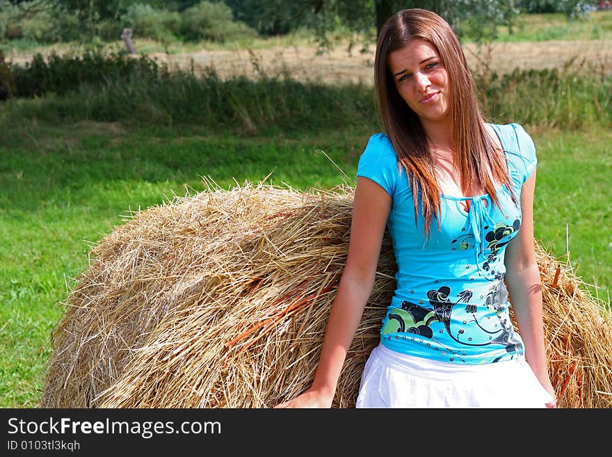 Young woman on the meadow in the summer behind a big bale of hay. Young woman on the meadow in the summer behind a big bale of hay