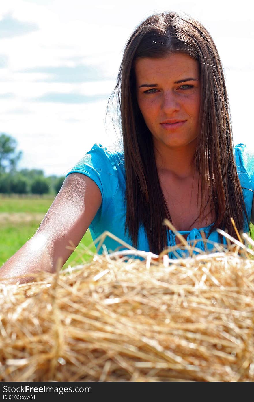 Young woman on the meadow in the summer behind a big bale of hay. Young woman on the meadow in the summer behind a big bale of hay