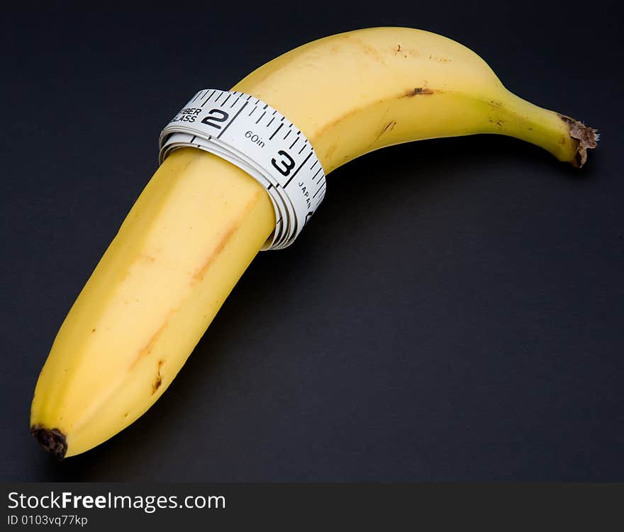 A banana with a tape measure wrapped around it isolated on a black background. A banana with a tape measure wrapped around it isolated on a black background.