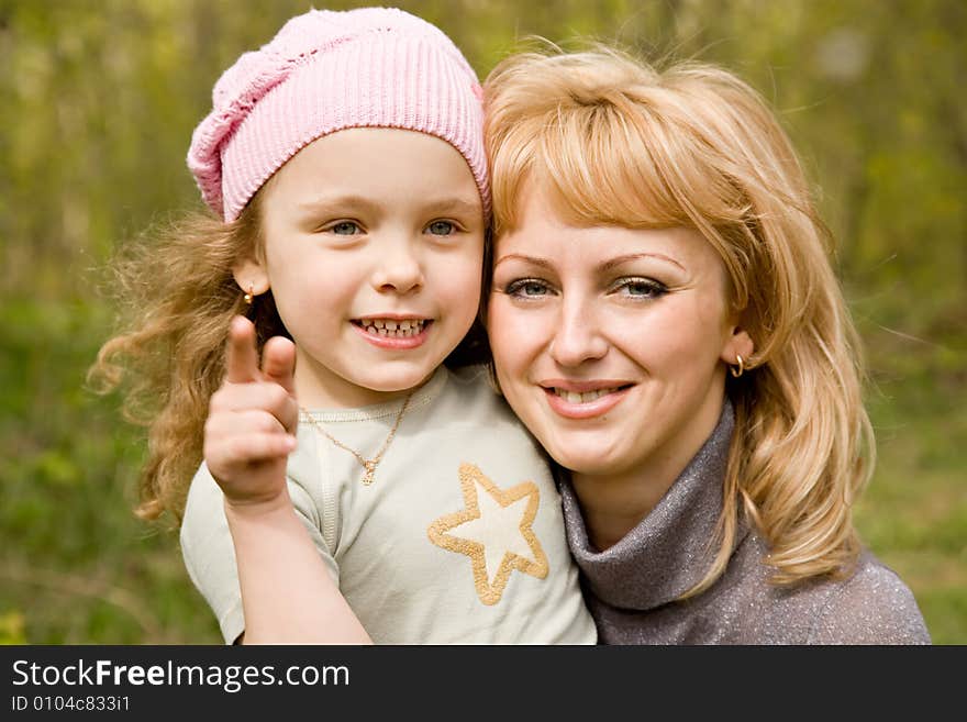 Small blond girl in a pink cap with mum shows a finger outdoors. Small blond girl in a pink cap with mum shows a finger outdoors