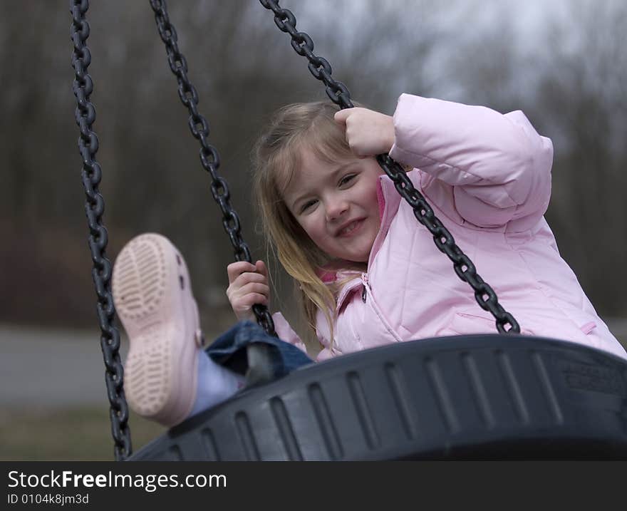 Happy 4 year old blond girl swinging on tire swing, outdoors