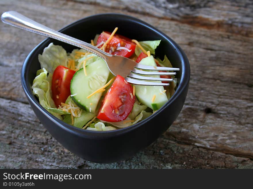 Fresh house salad in a black bowl with a fork.  All done on an old wood textured background.  Copy space also available.