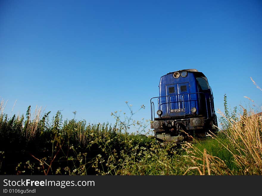 Blue train approaching between green field and blue sky