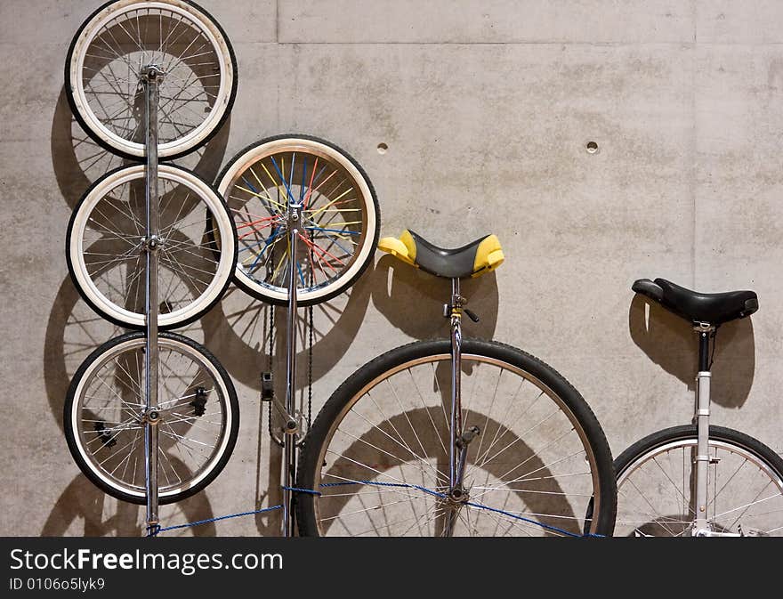 A variety of unicycles leaning against a cement wall