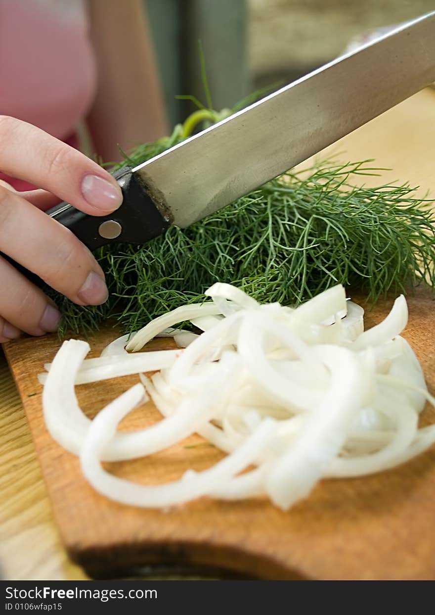 Female hand holding knife above board with dill and onion. Female hand holding knife above board with dill and onion