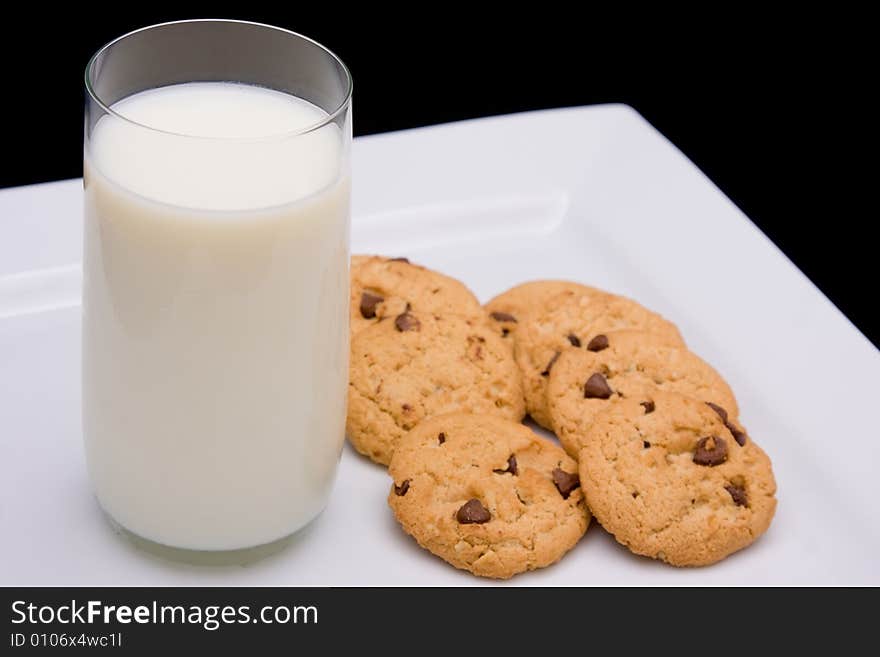 A glass of milk and half a dozen cookies on a plate against a black background. A glass of milk and half a dozen cookies on a plate against a black background