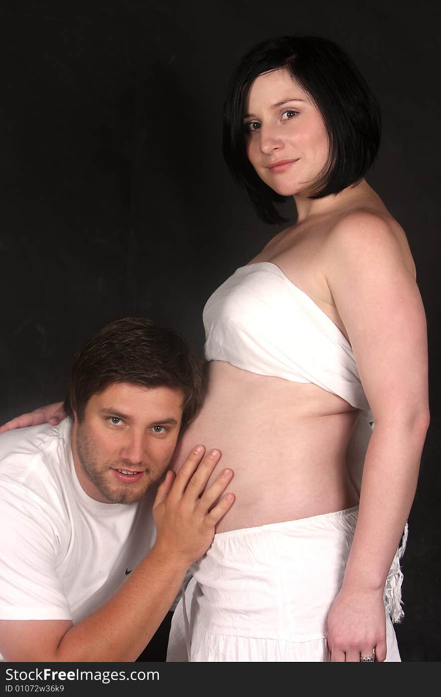 Young man listens to his baby by putting his ear next to his wife’s pregnant tummy. Young man listens to his baby by putting his ear next to his wife’s pregnant tummy.